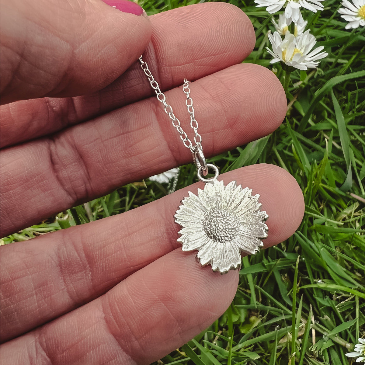 Hand holding silver daisy pendant on daisy field background