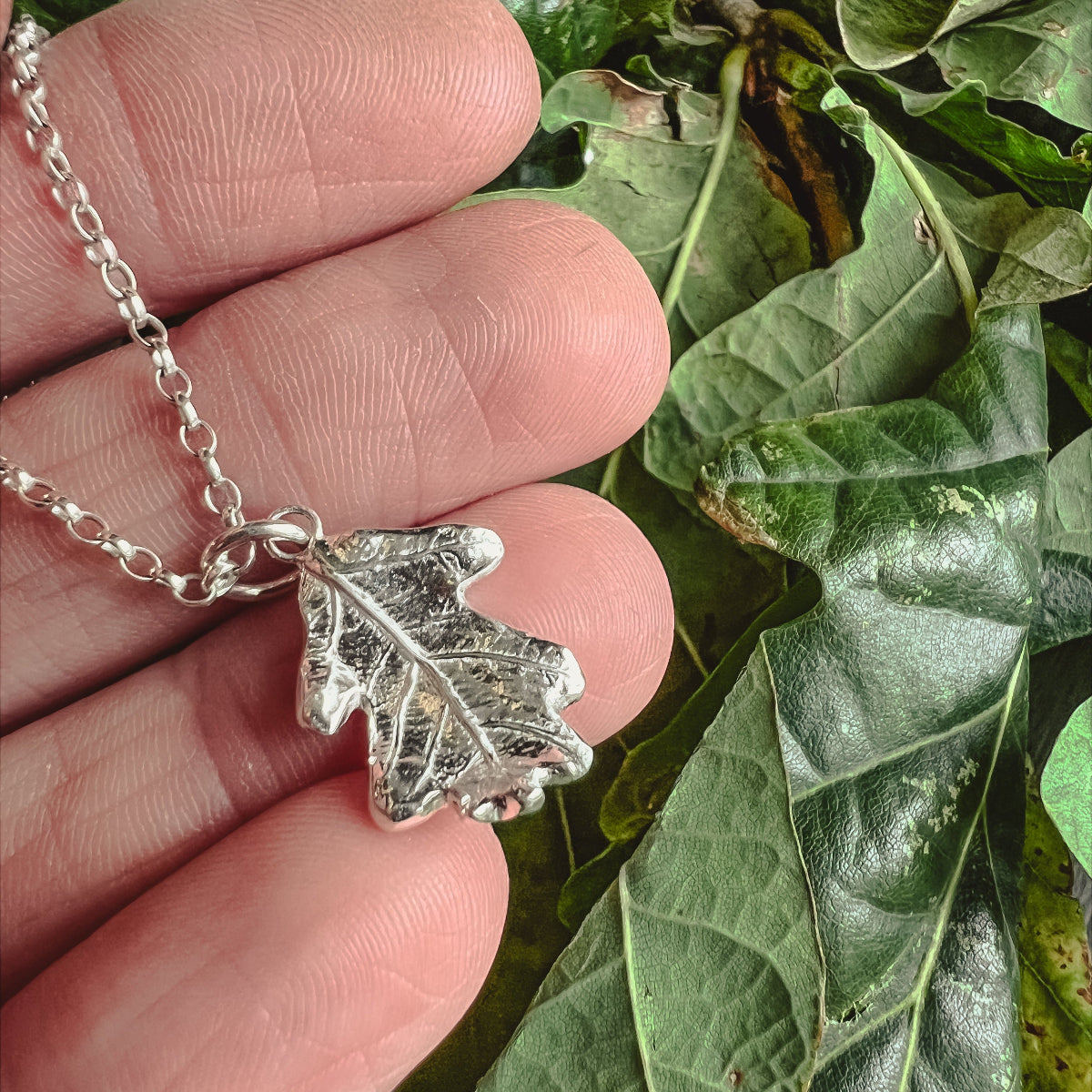 hand holding silver oak leaf necklace on green oak leaves