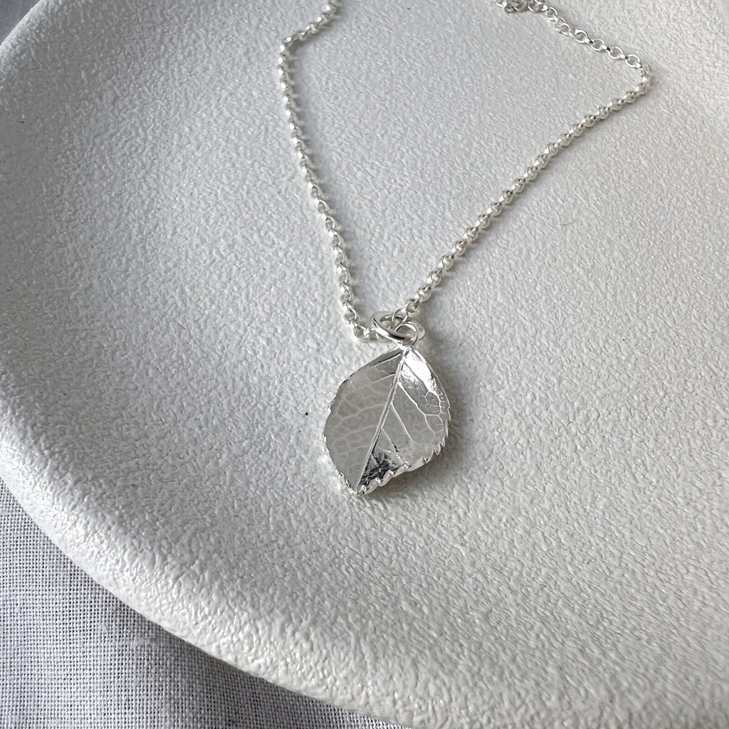 Silver rose leaf necklace on white plate