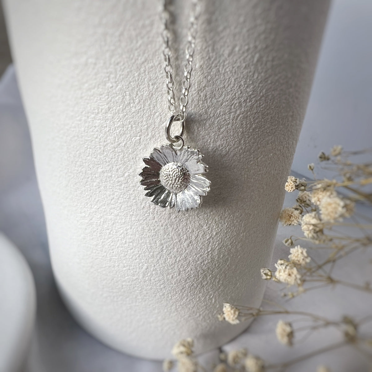 silver daisy necklace hanging from white vase and white flowers