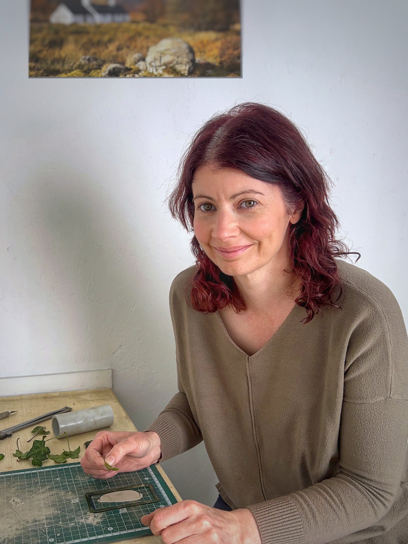 Lady sitting at work bench with ivy leaves and silver clay wearing green top