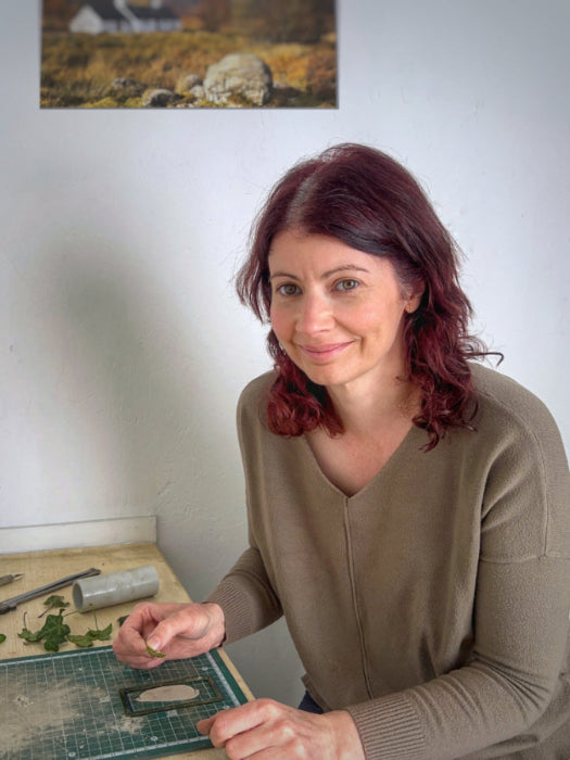 Lady sitting at work bench with ivy leaves and silver clay wearing green top
