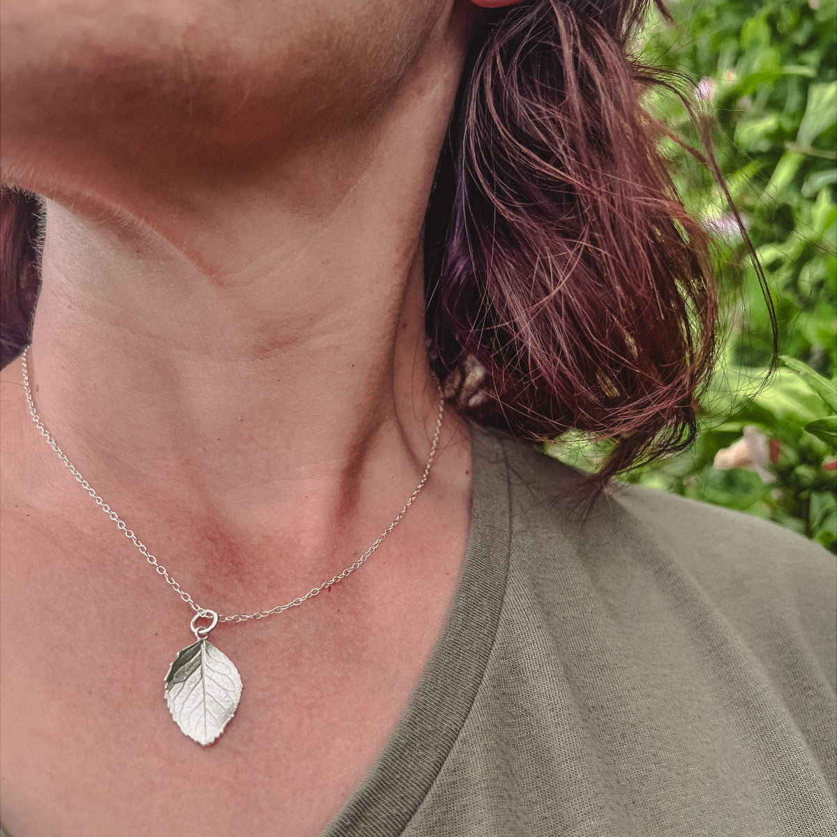 lady wearing silver leaf pendant and green top in countryside