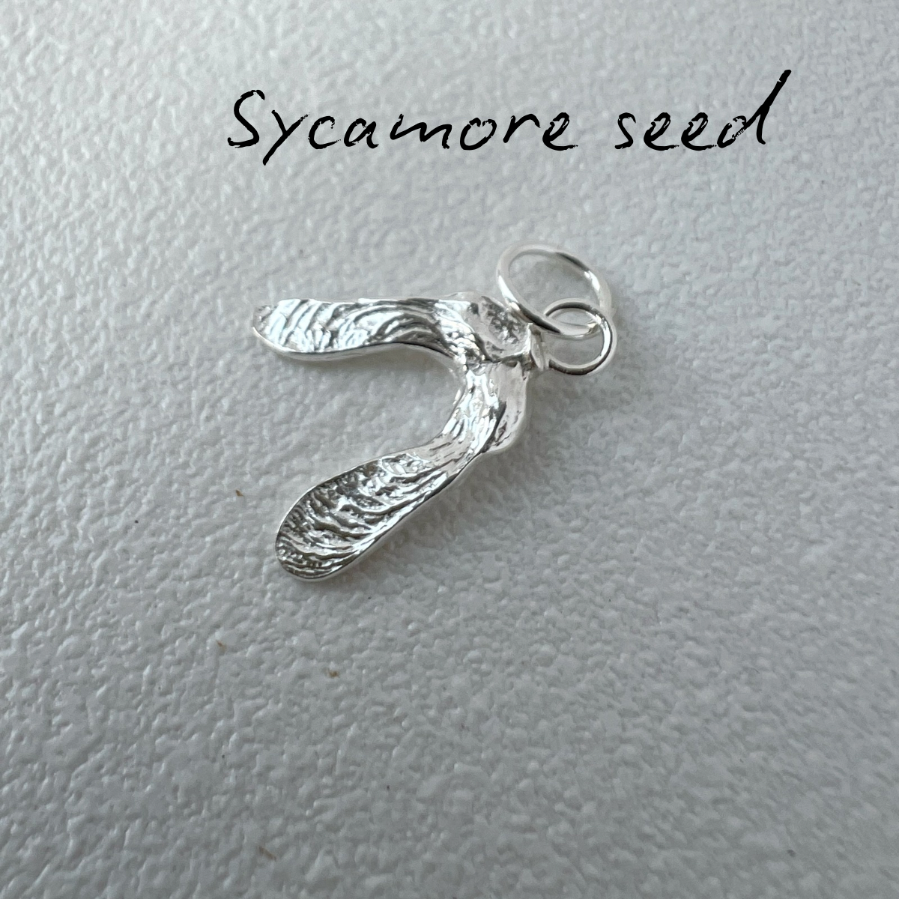 Silver sycamore seed pendant on a light gray background