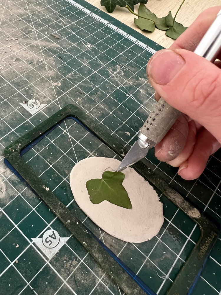 using a scaple to lift an ivy leaf off a piece of silver clay having taken an imprint