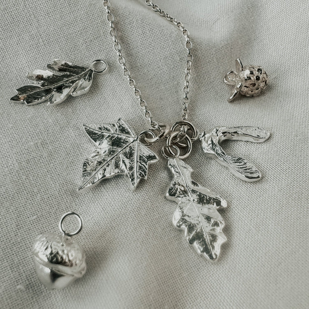 Silver leaf and acorn charm necklace on a light fabric background