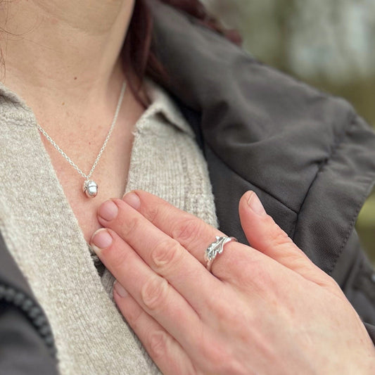 Close up of lady wearing cream jumper and black coat with silver acorn pendant and silver oak ring in countryside