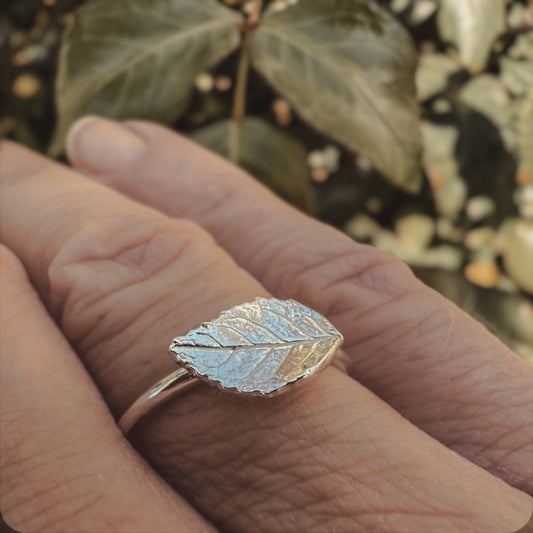 Tiny silver rose leaf ring on finger wih rose leaf background