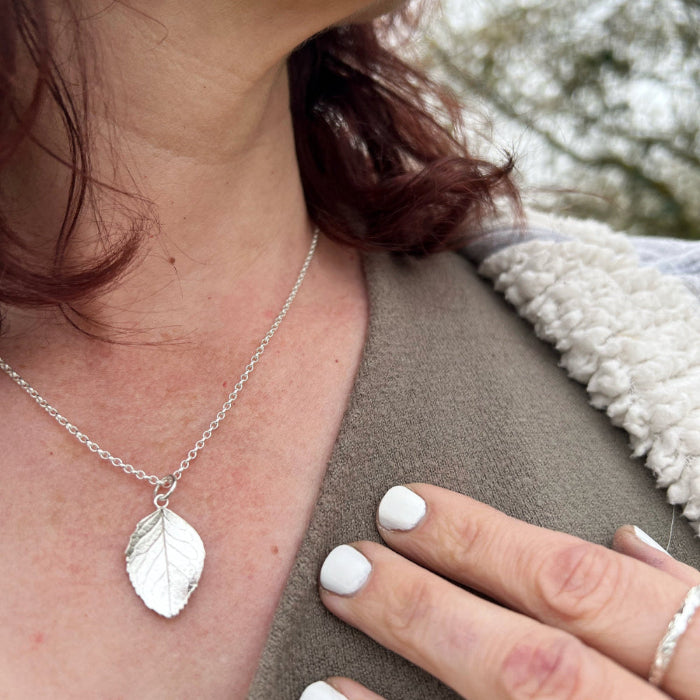 Close up of lady in countryside wearing green top and silver leaf pendant with white nail varnish