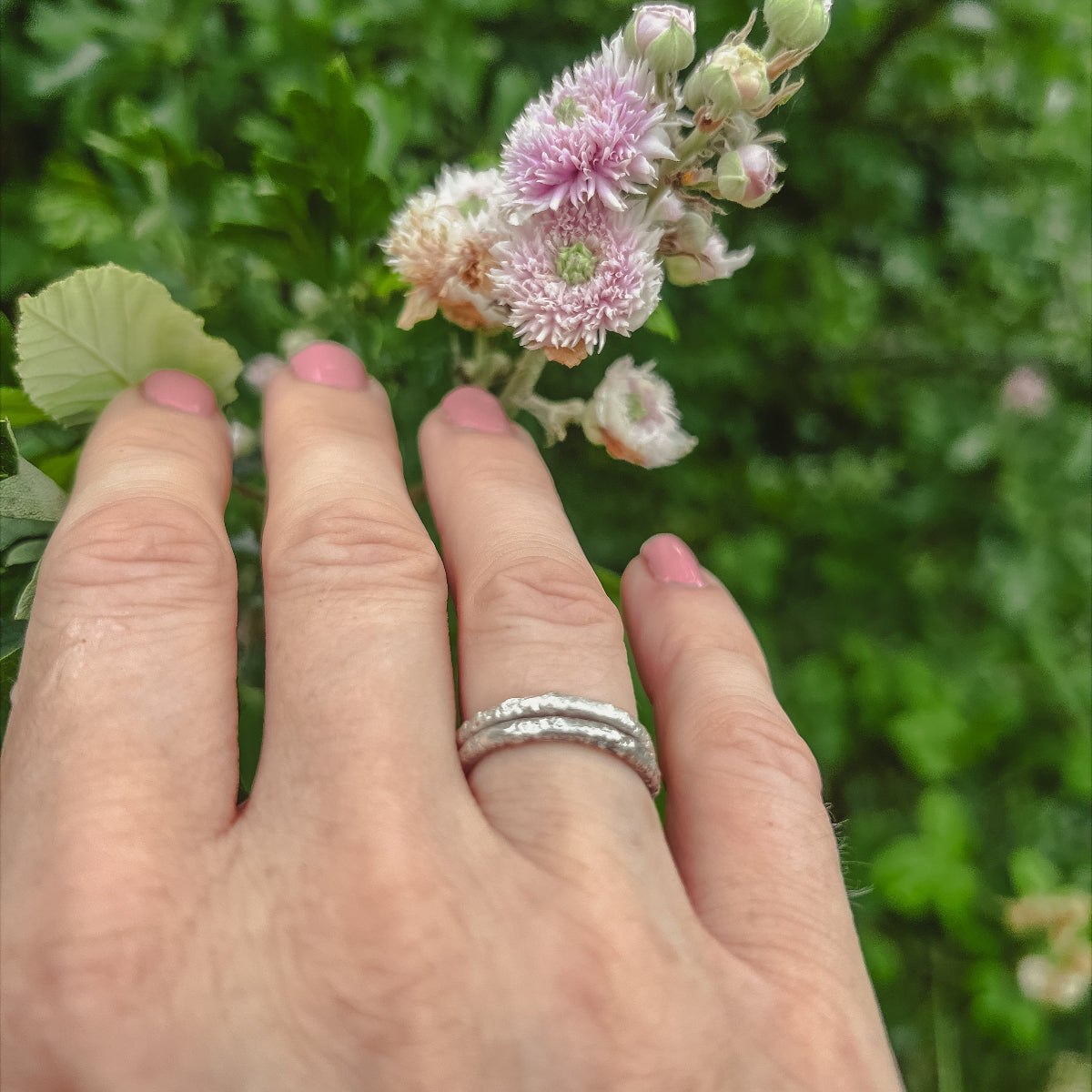 Hand wearing two textured silver stacking rings in countryside