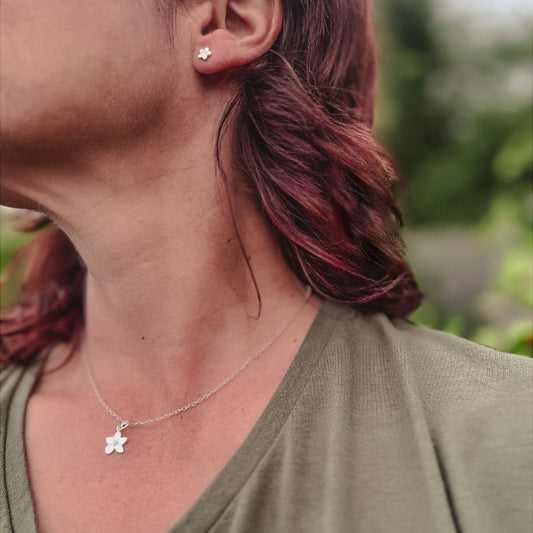 lady wearing silver forget me not necklace and earrings with green top in countryside
