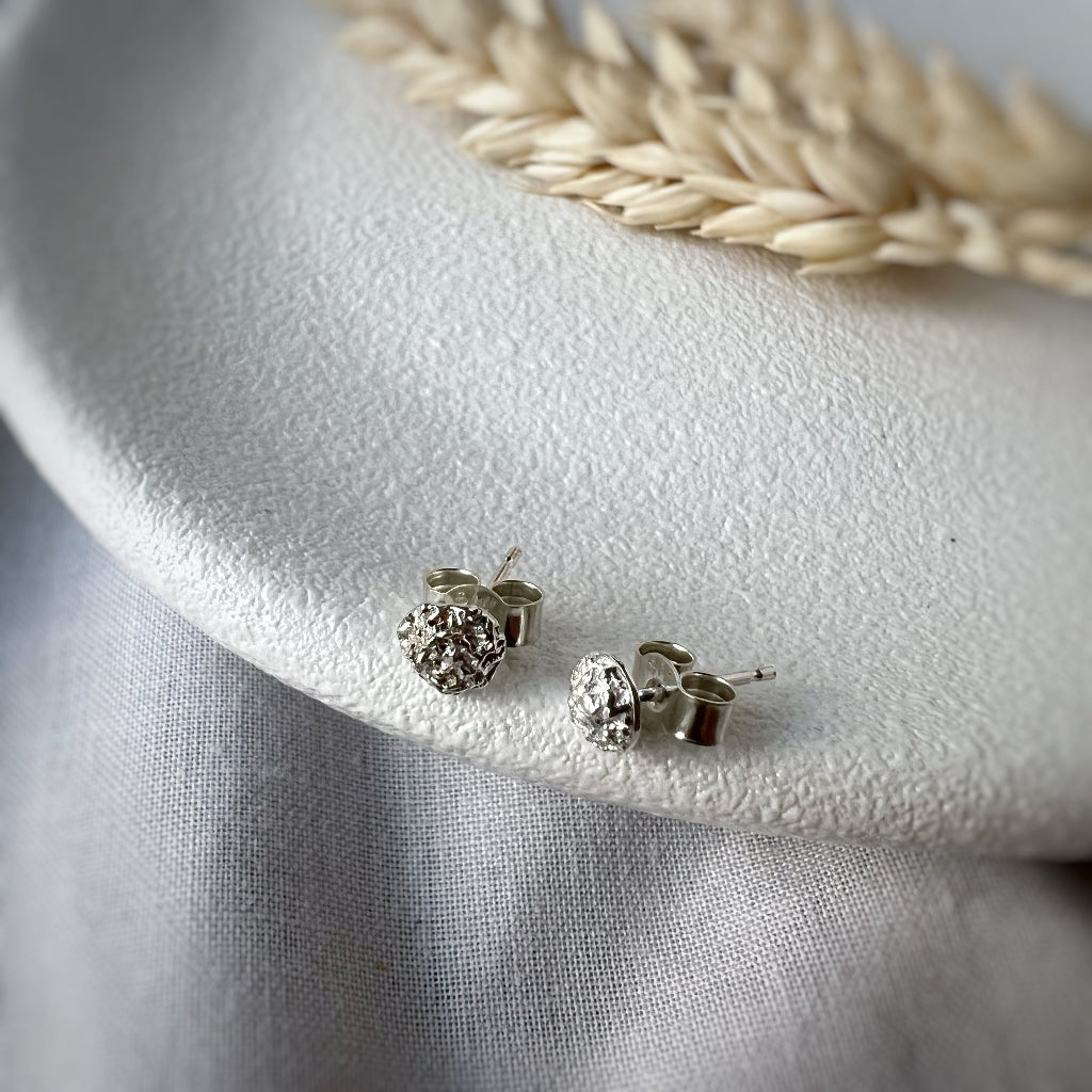 Small textured silver stud earrings on white plate