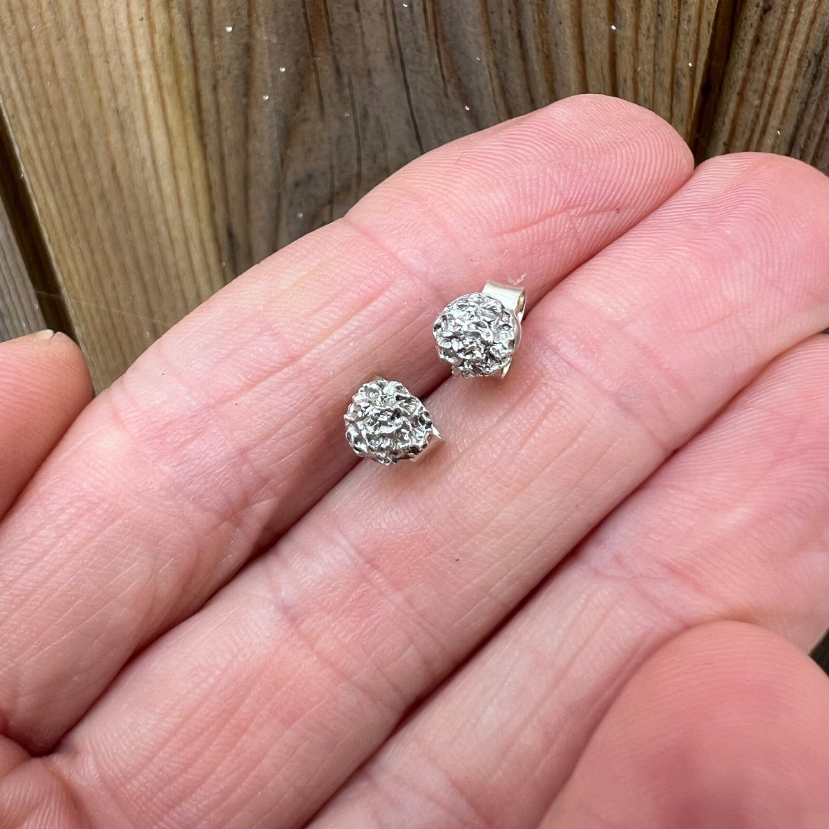 hand holding silver textured stud earrings against wood background