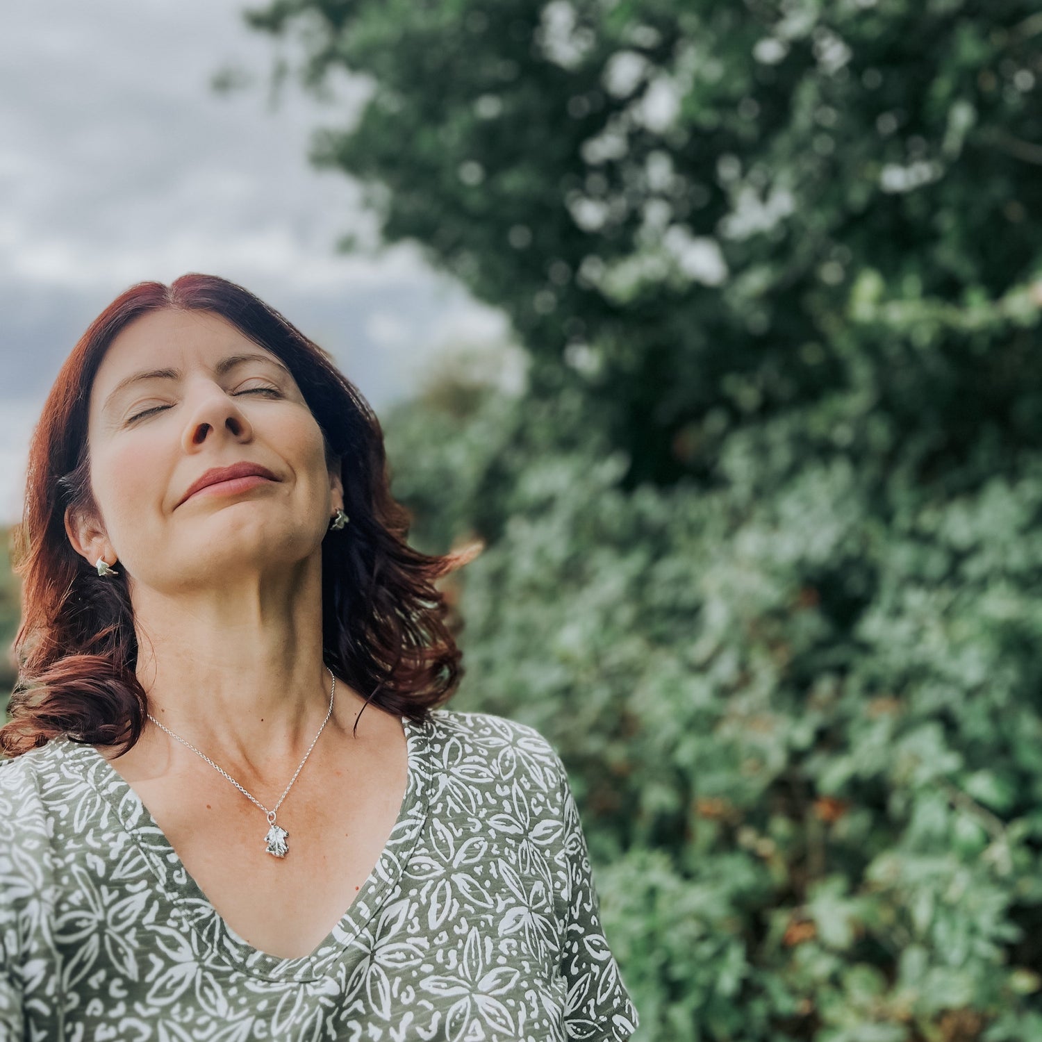 Woman outside eyes closed, wearing green dress and oak pendant