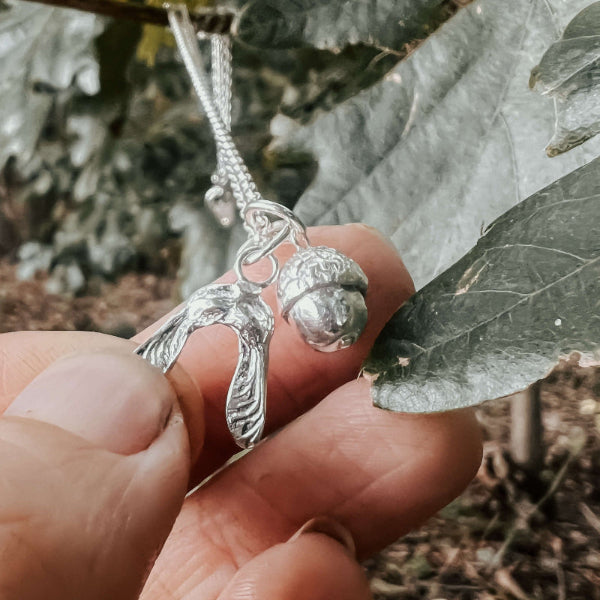 Silver necklace with a acorn and sycamore pendant held between leaves