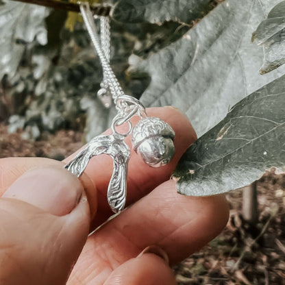 Silver necklace with a acorn and sycamore pendant held between leaves
