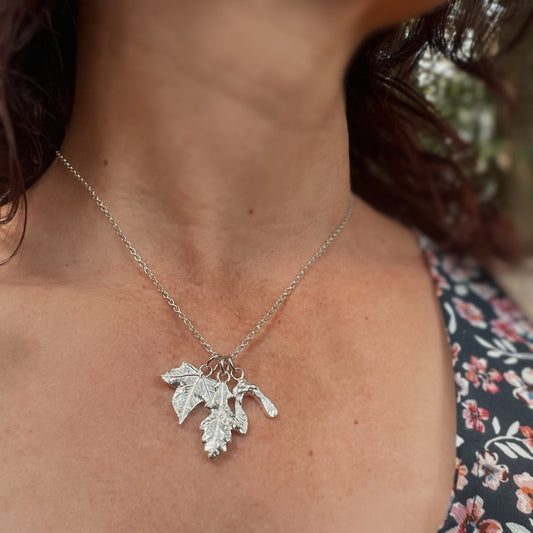Silver necklace with a leaf pendant worn by a person in a floral dress.