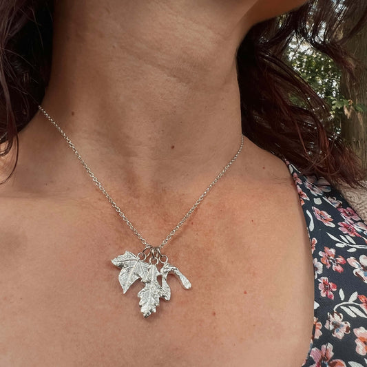 Silver necklace with maple and oak leaf pendant worn by a person outdoors