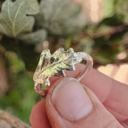 hand holding silver oak leaf ring with green leaves in background