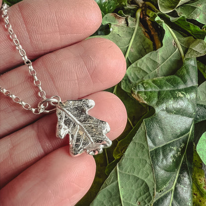 hand holding silver oak leaf necklace on green oak leaves