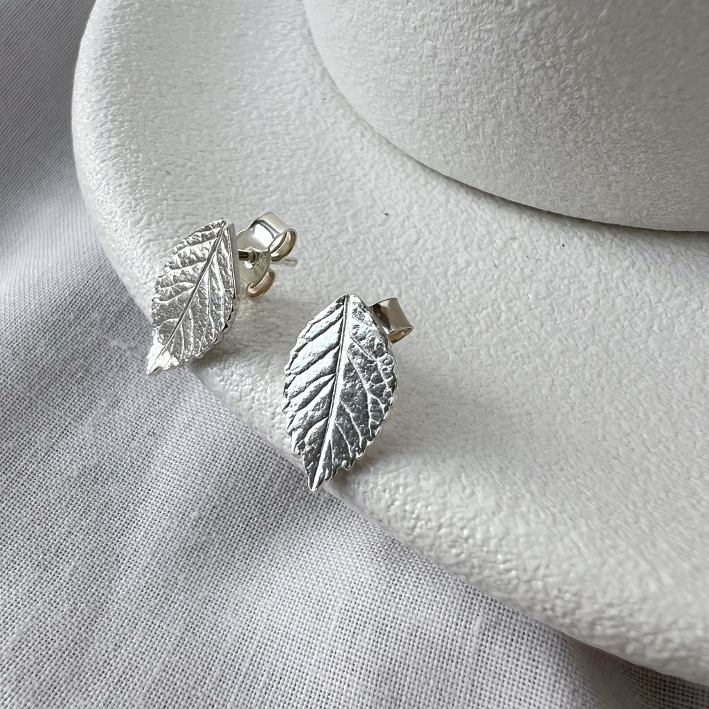 Silver rose leaf earrings on white plate