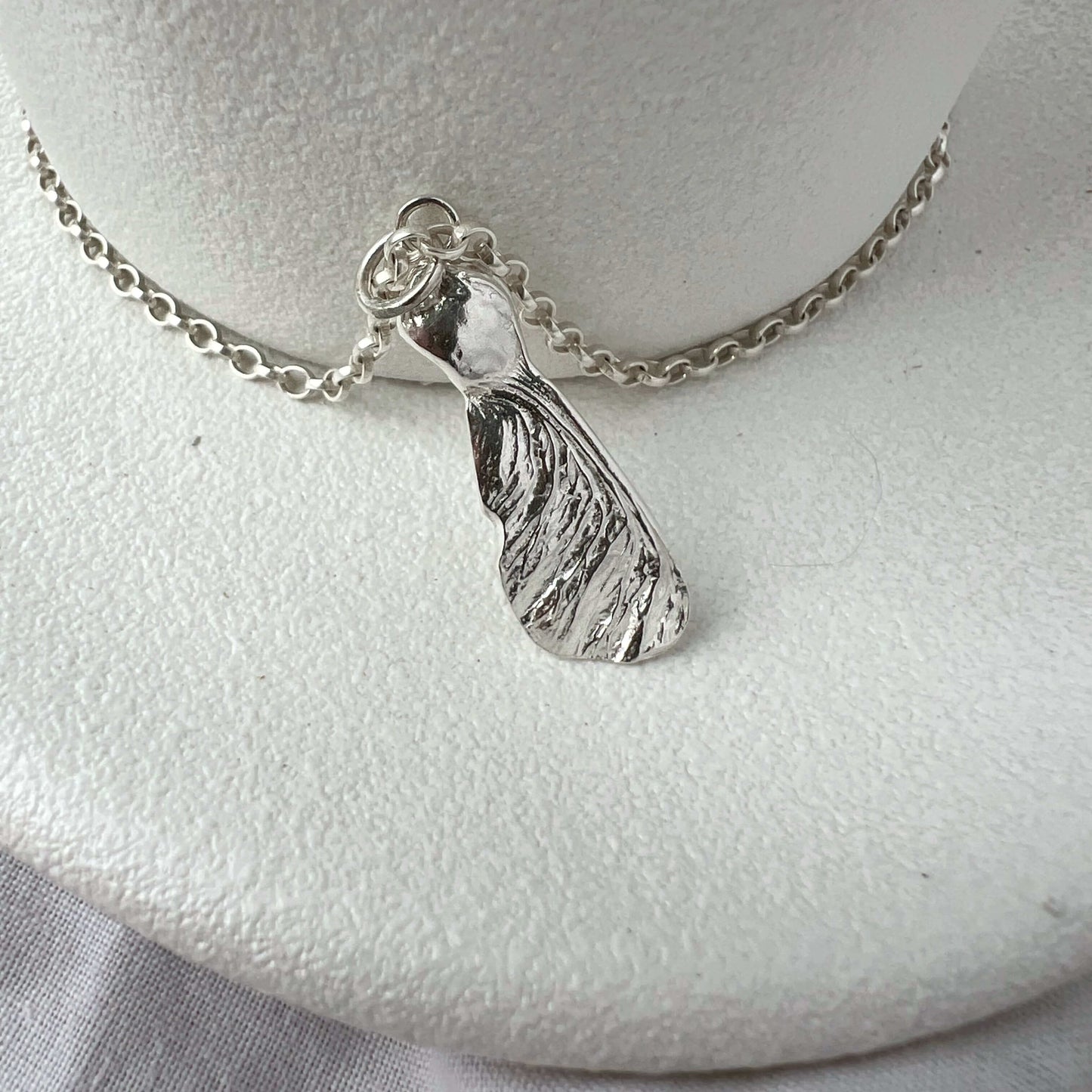 Silver seed pendant necklace on a white plate