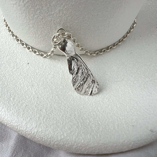 Silver seed pendant necklace on a white plate