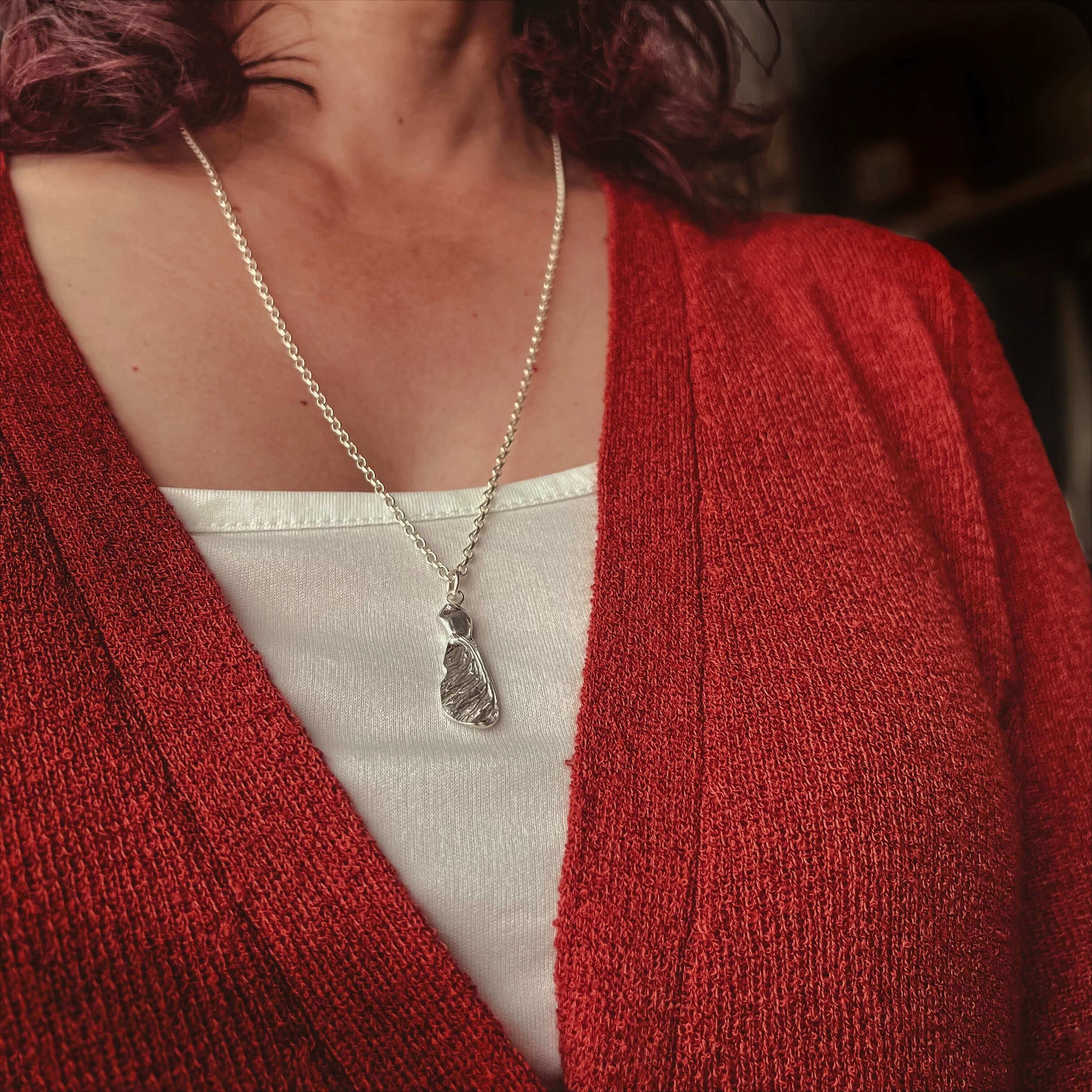 Person wearing a burn orange cardigan and white top with a silver necklace featuring a silver sycamore seed.