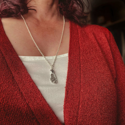 Person wearing a burn orange cardigan and white top with a silver necklace featuring a silver sycamore seed.