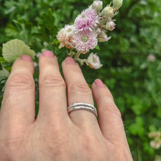 Hand wearing two textured silver stacking rings in countryside